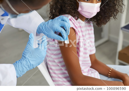 Doctor holds syringe and disinfects place on child's hand before vaccine injection. 100896590