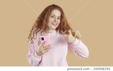 Cute young woman recommends use of new modern model of popular smartphone and mobile applications. 100896595