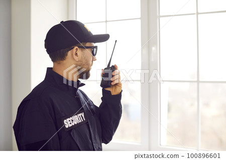 Security guard standing inside house, looking out window, and using walkie talkie Security guard standing inside house, looking out window, and using walkie talkie 100896601