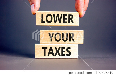 Lower your taxes symbol. Concept words Lower your taxes on wooden blocks on a beautiful grey table grey background. Businessman hand. Business tax lower your taxes concept. Copy space. 100896810