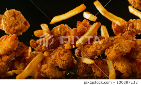 Freeze Motion Shot of Flying Fresh Fried Chicken Wings or Strips with French Fries, Close-up Freeze Motion Shot of Flying Fresh Fried Chicken Wings or Strips with French Fries, Close-up 100897138