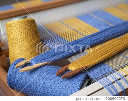 Blue and yellow striped weaving project on the hand loom. Weaving loom, shuttles and bobbins with threads 100900053