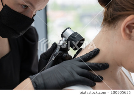A dermatologist examines a patient's mole through a dermatoscope.  100905635