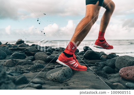 Running shoes of athlete man jogging on beach. Difficult terrain with wet rocks for training outdoors. Runner exercising Running shoes of athlete man jogging on beach. Difficult terrain with wet rocks for training outdoors. Runner exercising 100908551