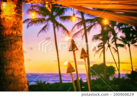 Hawaii luau party with fire torches at sunset. Hawaiian icon, lights burning at dusk at Waikiki beach resort restaurant for outdoor lighting cozy atmosphere 100908629