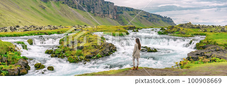 Iceland. Woman by waterfall on Iceland. Multiracial woman portrait in casual clothing visiting icelandic nature landscape Iceland. Woman by waterfall on Iceland. Multiracial woman portrait in casual clothing visiting icelandic nature landscape 100908669