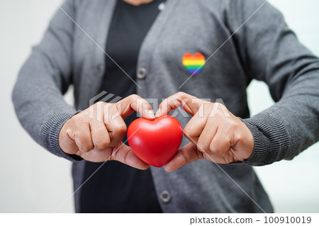 Asian woman holding red heart with rainbow flag, LGBT symbol rights and gender equality, LGBT Pride Month in June. 100910019