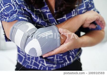 Asian senior woman wearing elastic support elbow brace for reduce pain. 100910569