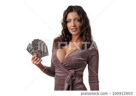Brunette girl in shiny dress posing holding fan of hundred dollar bills in her hand, standing isolated on white background. Casino, poker. Close-up. Brunette girl in shiny dress posing holding fan of hundred dollar bills in her hand, standing isolated on white background. Casino, poker. Close-up. 100912603