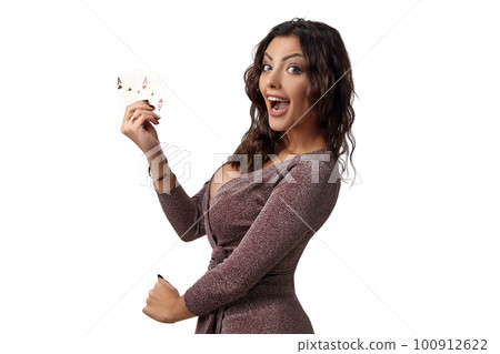 Brunette girl wearing shiny brown dress posing with two playing cards in her hand standing isolated on white background. Casino, poker. Close-up. Brunette girl wearing shiny brown dress posing with two playing cards in her hand standing isolated on white background. Casino, poker. Close-up. 100912622