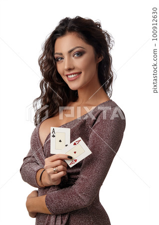 Brunette girl wearing shiny brown dress posing with two playing cards in her hand standing isolated on white background. Casino, poker. Close-up. Brunette girl wearing shiny brown dress posing with two playing cards in her hand standing isolated on white background. Casino, poker. Close-up. 100912630