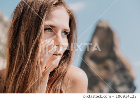 Woman summer travel sea. Happy tourist enjoy taking picture outdoors for memories. Woman traveler posing on the beach at sea surrounded by volcanic mountains, sharing travel adventure journey 100914122