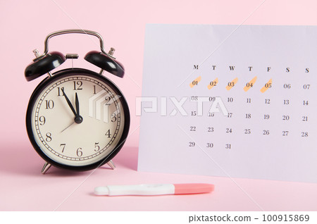 Still life with a black vintage alarm clock, calendar with days of the last menstruation marked and positive inkjet pregnancy test on pink pastel background. Rapid diagnosis of pregnancy at home Still life with a black vintage alarm clock, calendar with days of the last menstruation marked and positive inkjet pregnancy test on pink pastel background. Rapid diagnosis of pregnancy at home 100915869