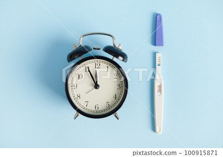 Still life with alarm clock and pregnancy test at work - the appearance of two stripes. Rapid diagnosis of pregnancy at home. Time of registration for pregnancy. Female health and fertility concept Still life with alarm clock and pregnancy test at work - the appearance of two stripes. Rapid diagnosis of pregnancy at home. Time of registration for pregnancy. Female health and fertility concept 100915871