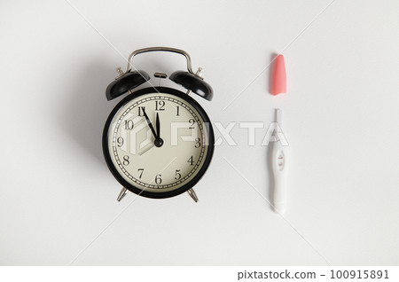 Still life with black vintage alarm clock and inkjet positive pregnancy test on isolated white background. Concept of pregnancy, motherhood and anticipation of a baby. Women's health and fertility Still life with black vintage alarm clock and inkjet positive pregnancy test on isolated white background. Concept of pregnancy, motherhood and anticipation of a baby. Women's health and fertility 100915891