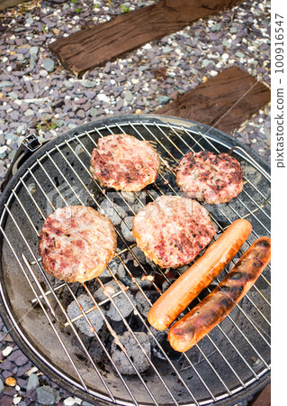 Hamburgers and frankfurters being grilled on the barbecue stove 100916547