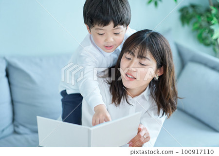 父母和孩子坐在沙發上，看一本圖畫書 100917110