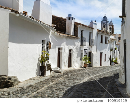 Ancient cobblestone alley with traditional white houses in Monsaraz, walled medieval village in Portuguese Alentejo region near the border with Spain 100919329