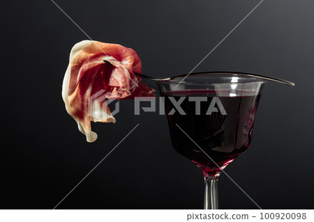 Spanish jamon or Italian prosciutto on a fork and a glass of red wine. Spanish jamon or Italian prosciutto on a fork and a glass of red wine. 100920098