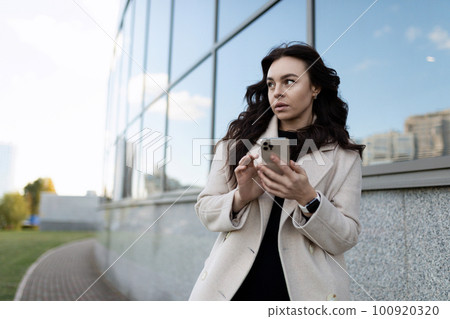 young adult woman with a phone in her hands on the background of the university 100920320