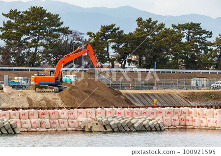 Red excavator working on river bank 100921595