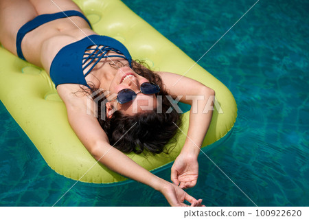 A beautiful girl in sunglasses is sunbathing on an air mattress in the pool during her vacation 100922620