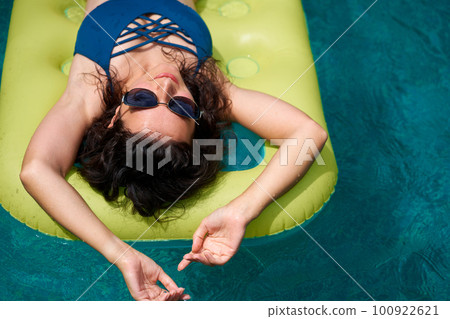 A beautiful girl in sunglasses is sunbathing on an air mattress in the pool during her vacation 100922621