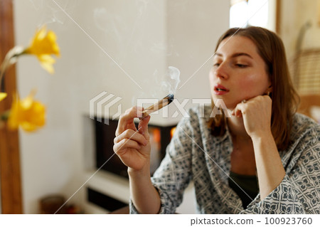 Woman hands burning Palo Santo, before ritual on the table with candles and green plants. Smoke of smudging treats pain and stress, clears negative energy and meditation wooden stick Woman hands burning Palo Santo, before ritual on the table with candles and green plants. Smoke of smudging treats pain and stress, clears negative energy and meditation wooden stick 100923760
