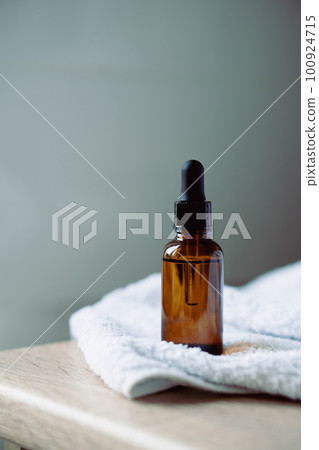 Amber glass serum oil dropper bottle and white towel on table mock-up, cosmetic container daylight shot Amber glass serum oil dropper bottle and white towel on table mock-up, cosmetic container daylight shot 100924715
