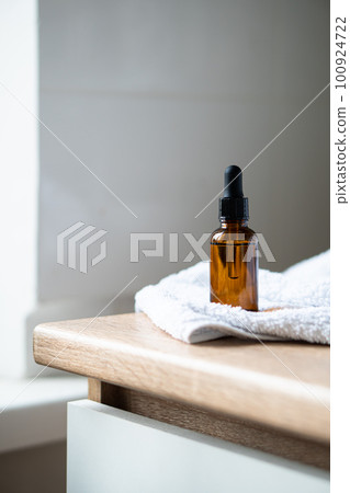 Amber glass serum oil dropper bottle and white towel on table mock-up, cosmetic container daylight shot 100924722