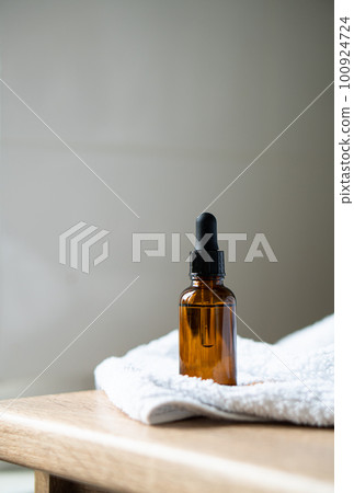Amber glass serum oil dropper bottle and white towel on table mock-up, cosmetic container daylight shot 100924724