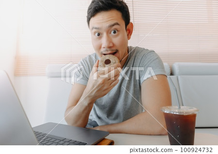Man eating cookies and iced americano coffee while working in the cafe. 100924732