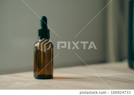 Amber glass serum oil dropper bottle on wooden table mock-up, cosmetic container daylight shot 100924733