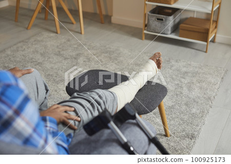 Young African American man with an injured leg and foot sitting on the couch at home Young African American man with an injured leg and foot sitting on the couch at home 100925173