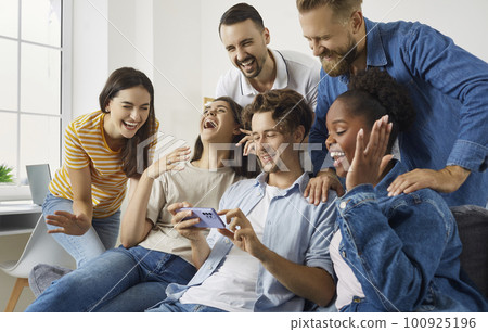 Happy diverse friends laughing as they watch something very funny on mobile phone 100925196