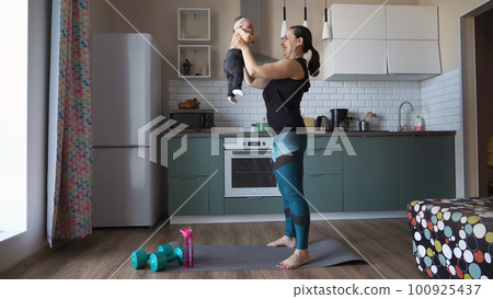 Sporty young mother is engaged with child in fitness exercises, woman doing squats at home Sporty young mother is engaged with child in fitness exercises, woman doing squats at home 100925437