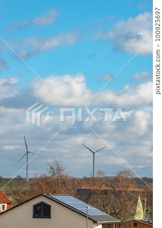 View over beautiful farm landscape with early spring agriculture field, wind turbines to produce green energy and a solar panels at the house roof in Mittweida, Germany, at blue sunny sky View over beautiful farm landscape with early spring agriculture field, wind turbines to produce green energy and a solar panels at the house roof in Mittweida, Germany, at blue sunny sky 100925697