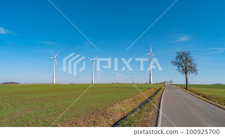 Panoramic view over beautiful farm landscape with early spring agriculture field, wind turbines to produce green energy and a lonely road near Mittweida, Germany, at blue sunny sky. 100925700