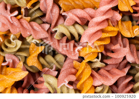 Rice vegetable pasta in the form of spirals, top view. Healthy rice pasta with tomatoes, selenera, carrots and beets 100925920