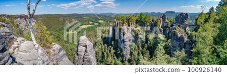 Panoramic over monumental Bastei sandstone pillars, rock formation and stacks surrounded by ancient forests at Kurort Rathen village in the national park Saxon Switzerland by Dresden, Saxony, Germany. Panoramic over monumental Bastei sandstone pillars, rock formation and stacks surrounded by ancient forests at Kurort Rathen village in the national park Saxon Switzerland by Dresden, Saxony, Germany. 100926140