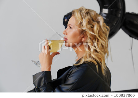 an attractive blonde in a black leather coat with a glass of champagne.  100927800