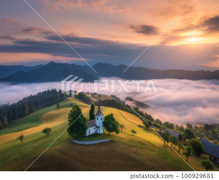 Aerial view of small church on the hill over pink low clouds 100929681