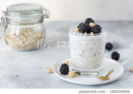 overnight oats with coconut milk, chia seeds, hazelnuts and blackberries on a gray background. healthy diet breakfast. copy space. horizontal image 100930698
