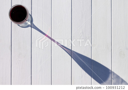 A glass of red wine and its long shadow on a white plank background. Top view. Copy space 100931212