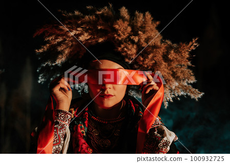 Ukrainian woman ties red ribbon around eyes as on ritual doll motanka. 100932725