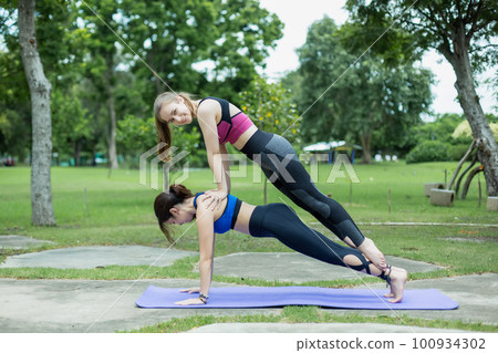 Two young attractive beautiful female wearing sportswear yoga pose in morning park nature. Two young attractive beautiful female wearing sportswear yoga pose in morning park nature. 100934302