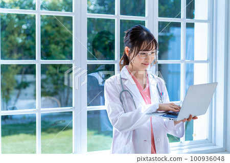 年輕的女醫生在窗邊使用筆記本電腦 100936048