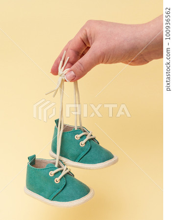 Woman holding newborn baby tiny shoes with laces on yellow background 100936562