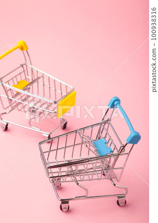 Mini shopping trolleys on pink background. Vertical photo Mini shopping trolleys on pink background. Vertical photo 100938316