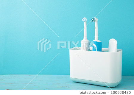 Holder with modern electric toothbrushes on blue background 100938480